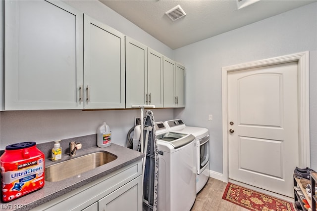 laundry room featuring separate washer and dryer, light hardwood / wood-style floors, sink, a textured ceiling, and cabinets