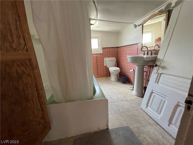 bathroom featuring tile walls, shower / bath combination with curtain, toilet, and tile floors