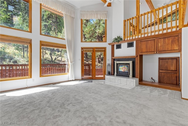 unfurnished living room with a healthy amount of sunlight, a high ceiling, light carpet, and a tile fireplace