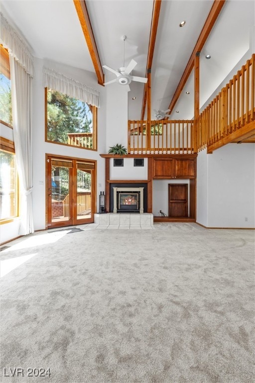 unfurnished living room with beamed ceiling, a high ceiling, a fireplace, light carpet, and ceiling fan