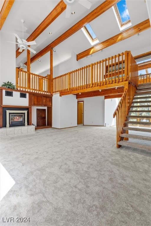 unfurnished living room with ceiling fan, a towering ceiling, a tile fireplace, and a skylight