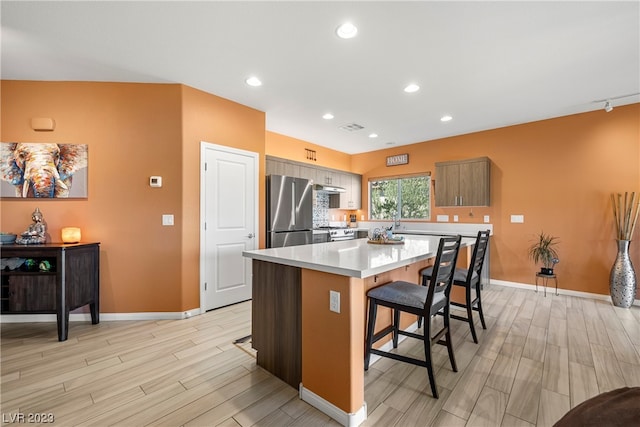 kitchen featuring light wood-type flooring, a center island, stainless steel refrigerator, and a breakfast bar area