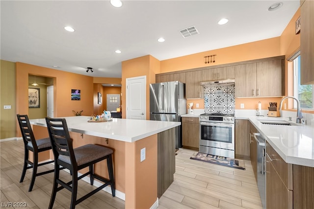 kitchen featuring sink, appliances with stainless steel finishes, a center island, a breakfast bar area, and light wood-type flooring