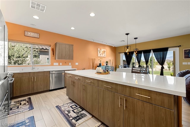 kitchen featuring sink, rail lighting, hanging light fixtures, stainless steel dishwasher, and light wood-type flooring