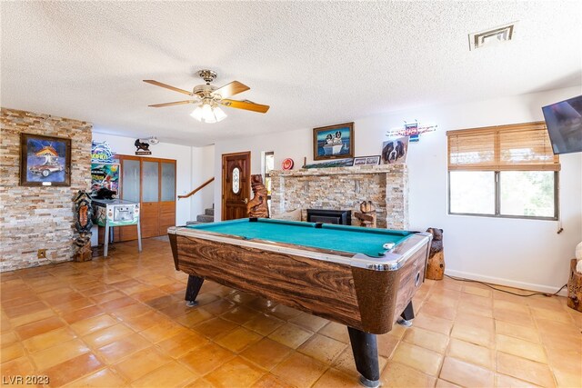 recreation room with light tile floors, a textured ceiling, a stone fireplace, and pool table