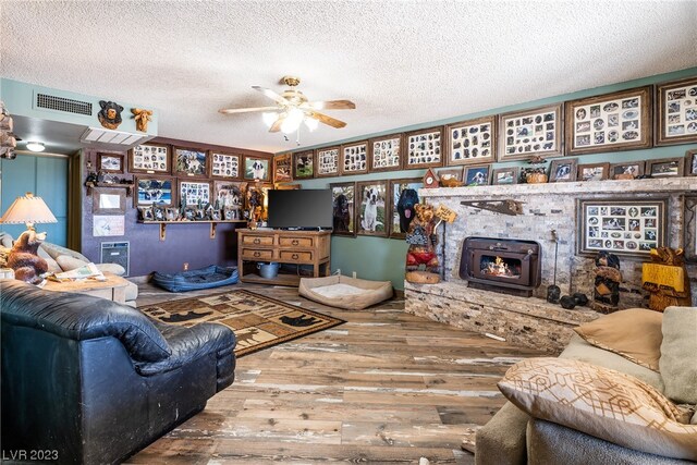 living room featuring ceiling fan, a textured ceiling, a wood stove, and hardwood / wood-style flooring