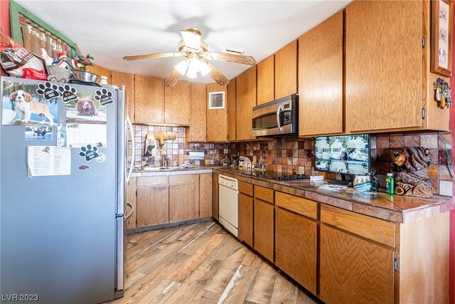 kitchen with backsplash, light hardwood / wood-style flooring, stainless steel appliances, and ceiling fan