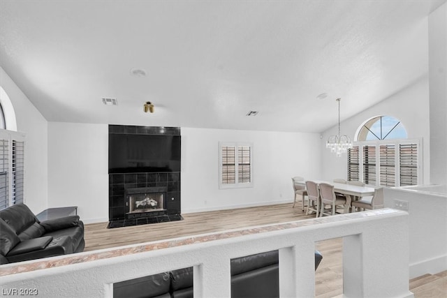 living room with lofted ceiling, a tile fireplace, light hardwood / wood-style flooring, and a notable chandelier