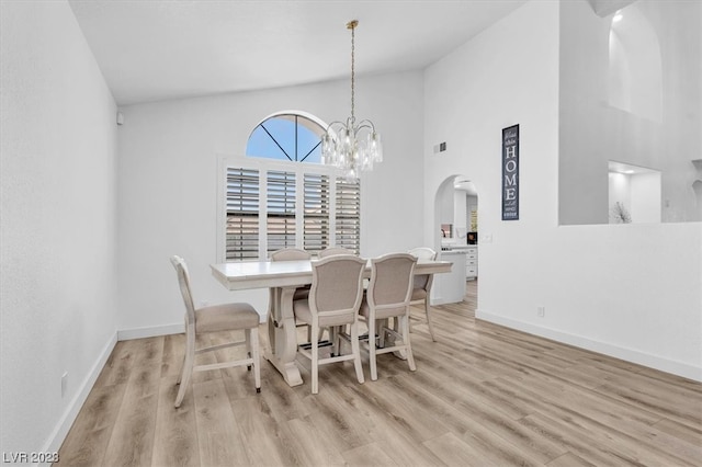 dining area with a high ceiling, a notable chandelier, and light wood-type flooring