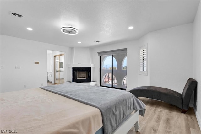 bedroom featuring access to exterior, light wood-type flooring, and a fireplace