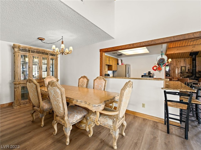 dining space with a textured ceiling, a wood stove, wood-type flooring, and an inviting chandelier