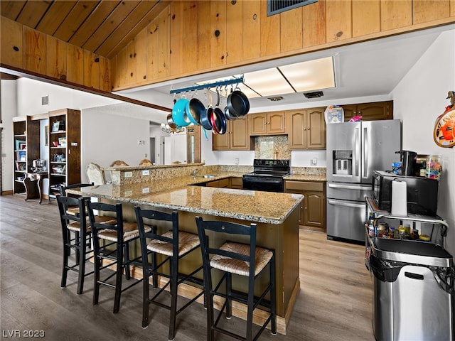 kitchen with a breakfast bar area, light wood-type flooring, light stone countertops, lofted ceiling, and black range with electric stovetop