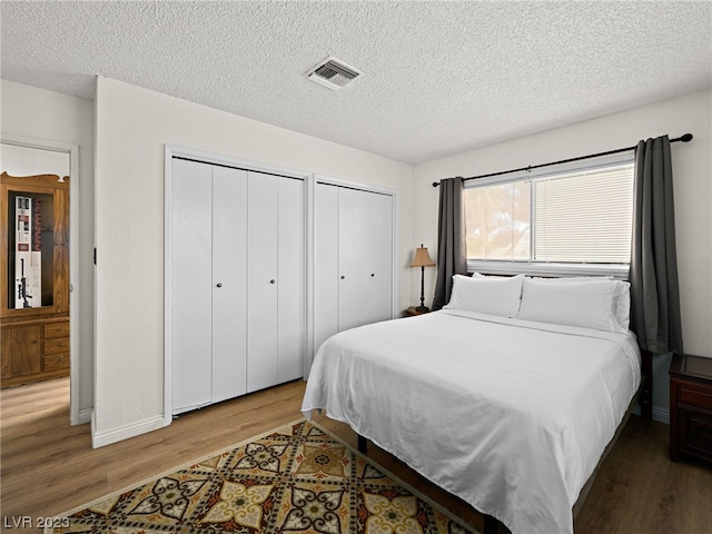 bedroom featuring a textured ceiling, two closets, and wood-type flooring