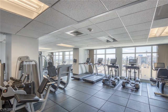 gym featuring dark tile flooring, a paneled ceiling, and expansive windows