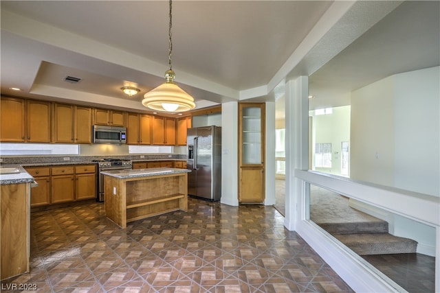 kitchen featuring decorative light fixtures, appliances with stainless steel finishes, a center island, dark tile flooring, and a tray ceiling