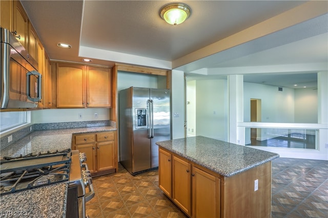 kitchen with stainless steel appliances, a kitchen island, a tray ceiling, and dark stone counters