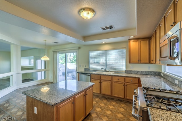 kitchen with a kitchen island, dark stone counters, appliances with stainless steel finishes, hanging light fixtures, and sink