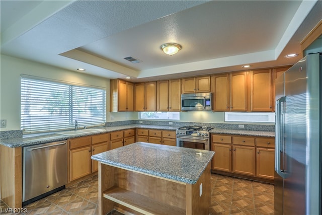 kitchen with sink, dark stone counters, a raised ceiling, stainless steel appliances, and a center island