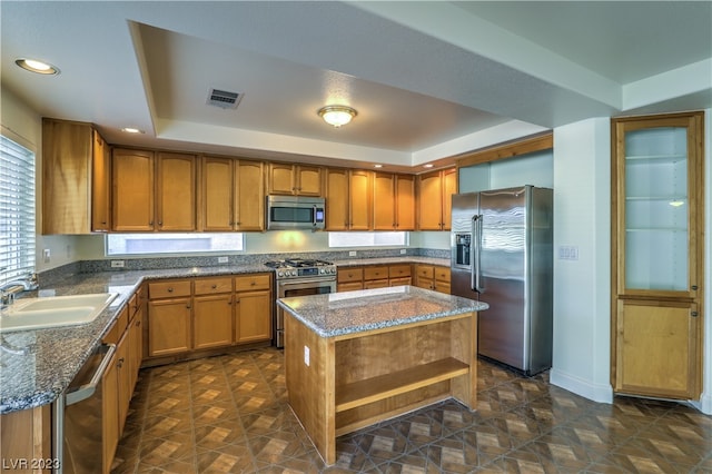 kitchen with a kitchen island, appliances with stainless steel finishes, dark stone countertops, and sink