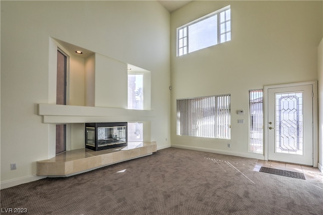 unfurnished living room with a healthy amount of sunlight, carpet flooring, a towering ceiling, and a tiled fireplace