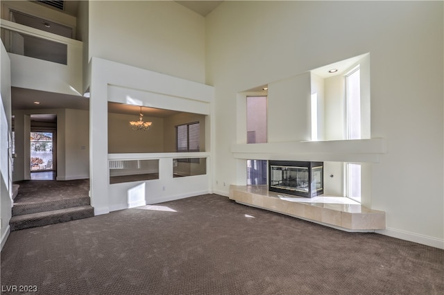 unfurnished living room with dark colored carpet, a high ceiling, a notable chandelier, and a fireplace