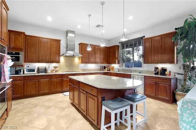 kitchen featuring pendant lighting, light tile floors, a kitchen island, stainless steel appliances, and wall chimney range hood