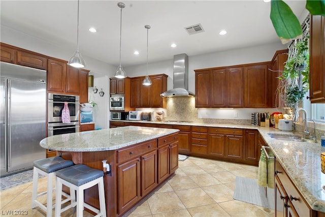 kitchen with pendant lighting, light stone counters, stainless steel appliances, wall chimney exhaust hood, and a center island