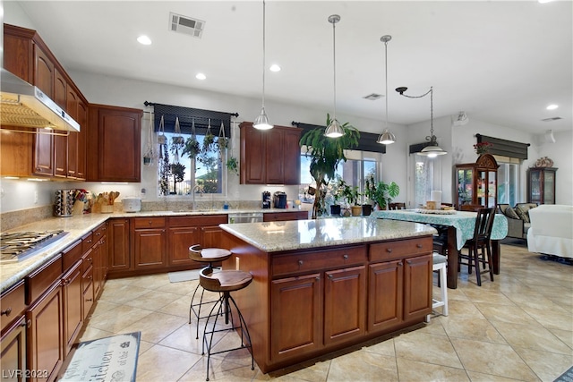 kitchen with hanging light fixtures, stainless steel appliances, wall chimney range hood, a kitchen bar, and a center island