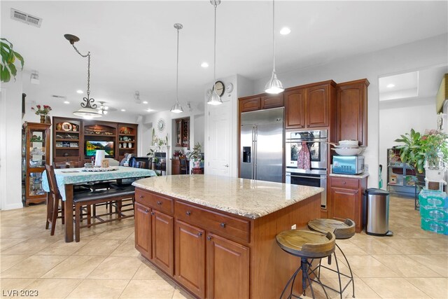 kitchen with stainless steel appliances, light tile floors, a kitchen island, decorative light fixtures, and light stone counters