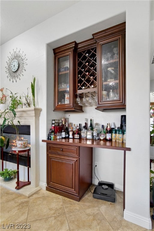 bar featuring a fireplace, dark brown cabinetry, and light tile floors