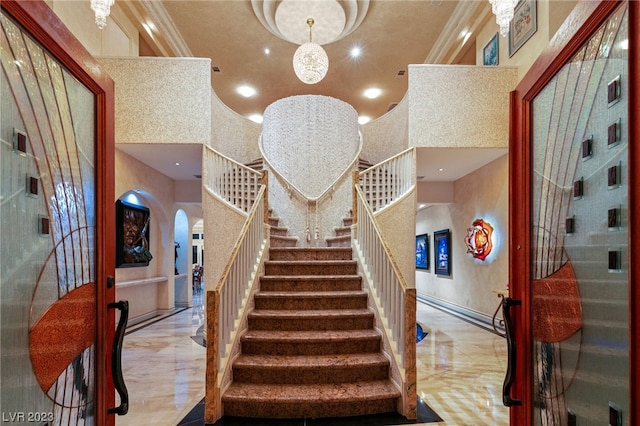 stairway featuring french doors, a towering ceiling, an inviting chandelier, and crown molding