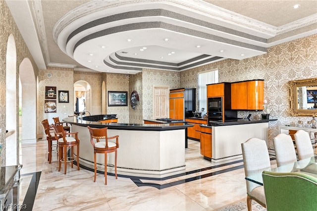 kitchen featuring ornamental molding, a raised ceiling, a spacious island, and black appliances