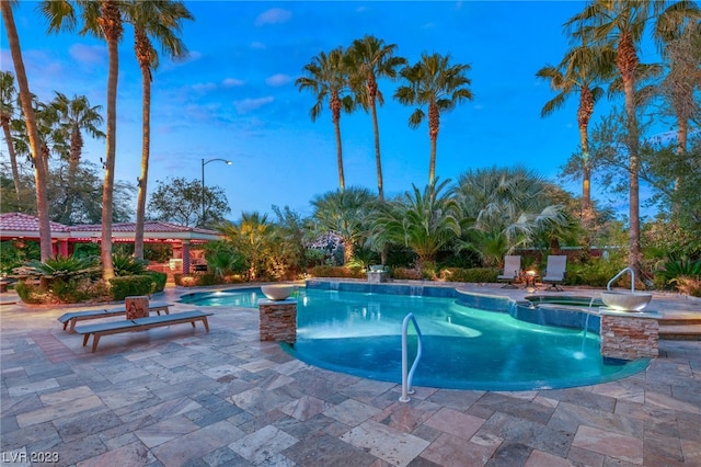 pool at dusk with a patio area, an in ground hot tub, and pool water feature