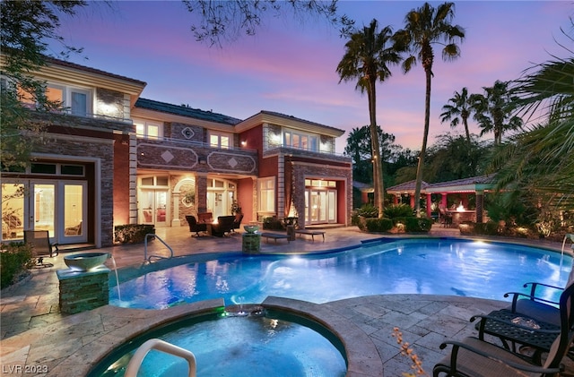 pool at dusk featuring a patio area and an in ground hot tub