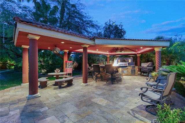 patio terrace at dusk featuring a gazebo, an outdoor kitchen, area for grilling, and an outdoor bar