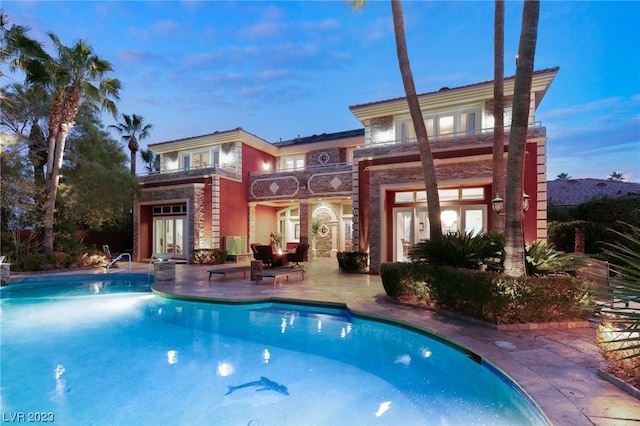 pool at dusk with french doors and a patio