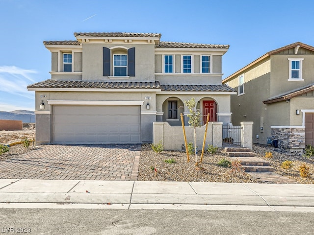 mediterranean / spanish house with a tiled roof, decorative driveway, an attached garage, and stucco siding