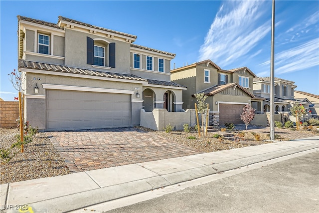 view of front of property featuring a tiled roof, an attached garage, fence, decorative driveway, and stucco siding