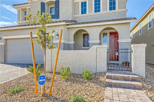 view of front of property featuring an attached garage, a fenced front yard, decorative driveway, and stucco siding