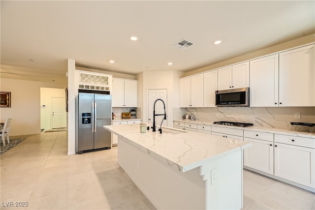 kitchen with tasteful backsplash, appliances with stainless steel finishes, white cabinetry, a sink, and an island with sink