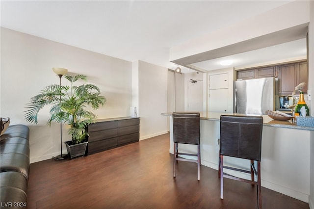 kitchen featuring stainless steel fridge, dark hardwood / wood-style flooring, a kitchen bar, and light stone counters