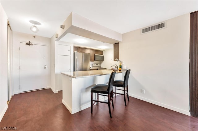 kitchen featuring stainless steel appliances, kitchen peninsula, a kitchen breakfast bar, light brown cabinetry, and dark hardwood / wood-style flooring