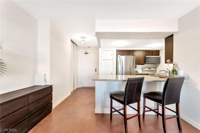 kitchen featuring appliances with stainless steel finishes, kitchen peninsula, hardwood / wood-style flooring, and a kitchen breakfast bar