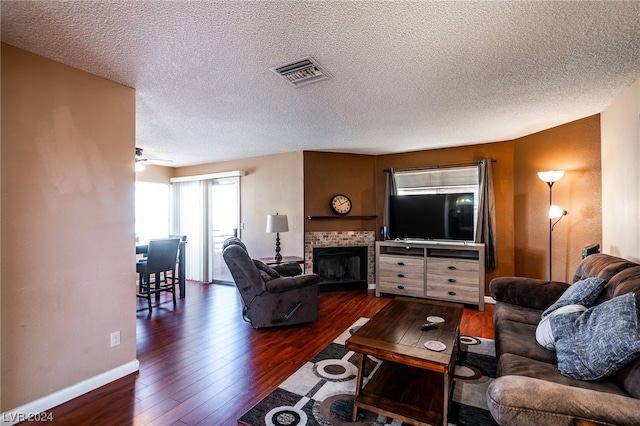 living room featuring a brick fireplace, dark wood-type flooring, and a textured ceiling