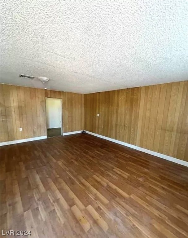 empty room featuring a textured ceiling, wood walls, and dark hardwood / wood-style floors