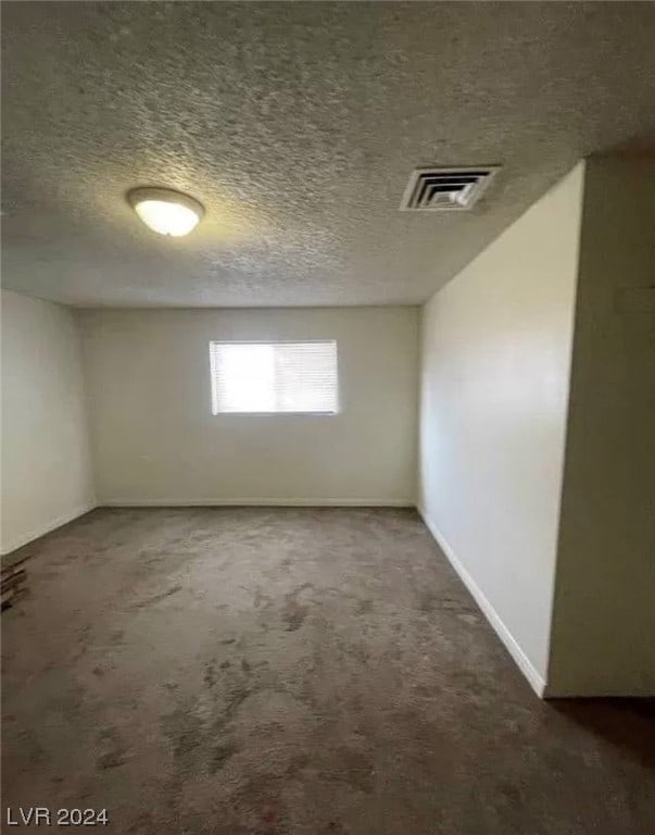 spare room with a textured ceiling and dark carpet