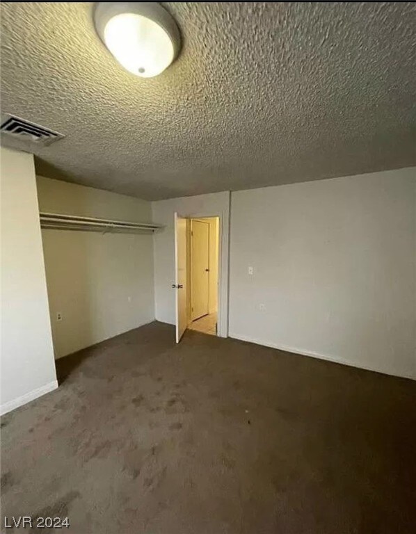 unfurnished bedroom with a closet, dark colored carpet, and a textured ceiling