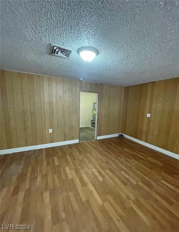 empty room with wood walls, a textured ceiling, and dark hardwood / wood-style flooring