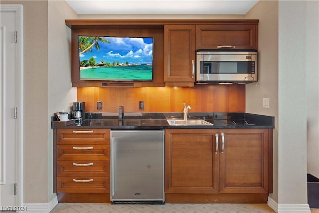 bar with sink, refrigerator, and dark stone counters