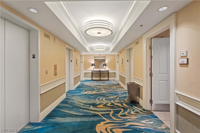 hall with a tray ceiling, elevator, crown molding, and light colored carpet